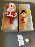 Both Santa and snowman toppers in their individual boxes, with packing materials visible.