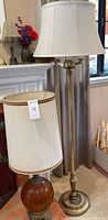 Brass floor lamp with tall slender design and four light bulbs, next to an amber glass table lamp with beige fabric shade