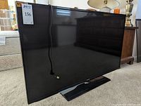 Front angled view of the Samsung 50 inch flat screen TV with base stand, power cord hanging in front, showing glossy black finish.