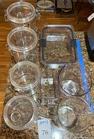 Top-down image showing four clear acrylic storage canisters with clip-lock lids, the rectangular acrylic Rubbermaid storage box with lid, and three measuring cups including a glass one on a kitchen counter.