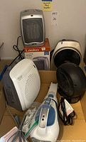 Lot of one hand-held vacuum, two portable fans, a Lasko ceramic heater with box, and a DeLonghi small portable heater, arranged on floor near wall with label.
