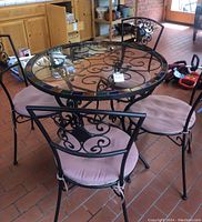 Glass and metal bistro table with tiled edging and four matching chairs with pink seat cushions viewed from an angle, showing overall set condition and materials.