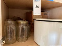 Shelf with several clear empty glass canning jars, some with metal lids and rings.