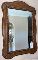 Full view of rectangular carved wood framed mirror with curved edges, showing the entire piece hanging on a wall.