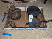 A photo of all four items including a large container, waffle iron, and an antique oil lamp, placed in two cardboard trays.