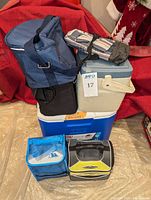 Multiple coolers and soft lunchboxes stacked together showing variety of items in the lot