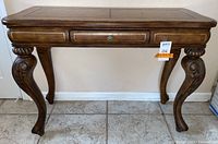 Front view of the carved wood entry table showing the center drawer, leather inset top, and the curved legs with detailed carvings.