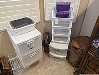 View of stacked plastic storage units with drawers, the tubs on top, and woven basket to the side