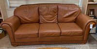 Front view of the three-seat gaucho leather couch with brass nail head trim showing overall condition.