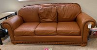 Front view of the gaucho leather couch with brass nail head detail, showing the three-seat cushions and rolled arms.