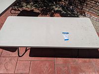 White rectangular folding table placed outdoors on a red concrete floor, showing entire surface and legs folded out.