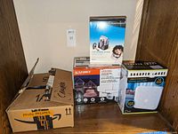 Photo showing boxed HP Photosmart 385 photo printer with power cord along with boxed Plantronics Voyager 510 Bluetooth headset, Sharper Image sleep sound machine, and Sunforce motion-activated LED light.