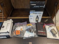 Photo showing Garmin GPSMAP 60CSx boxed device, Fitbit Versa boxes, solar chargers in plastic bags, SGB battery pack, SPOT Gen3 device and accessories.
