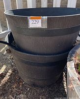Two black plastic barrel-style pots stacked, showing texture and size with dirt inside