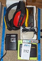Overhead shot showing all items including Sony Color Watchman, Sports Walkman, VOR tape recorder, iPod Shuffle, Casio cassette player, and protective ear covers arranged in a storage box.