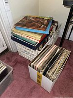 Photo showing multiple boxes with vinyl albums stacked inside and outside. Visible album covers on top include 'Carnival',