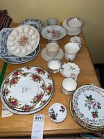 Wide view of the china collection arranged on a table showing a variety of plates, cups, and serving dishes including floral printed plates, egg serving plate, blue and white porcelain, and cups.