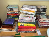 Wide view of multiple stacks of assorted books on a surface including some dictionaries and novels