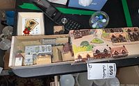View of LG flip phone, Wade of England miniature houses in original box, a small cameo frame, and a jar of assorted marbles on a table surface.