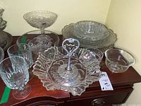 Overview photo showing a variety of crystal and glass serving dishes including a multi-section serving dish with a heart-shaped handle, pedestal bowl, stacked plates, stemmed glasses, and a small bowl.