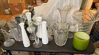 Overview of all vases on display table showing variety of crystal, milk glass, and ceramic items.