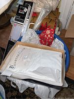 Blue bin containing boxed Harter Club luxury white tablecloth, white vintage cloth napkins, curtains in plastic bags, and boxed room darkening shades 29 x 64 inches.