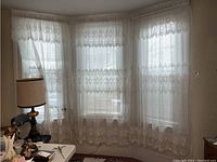 Wide view of the three sheer curtain panels installed on a three-window bay area, showing full length and lace detail.