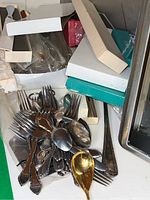 Photo showing assorted sterling forks and spoons with some serving pieces mixed in, with original packaging boxes in background.