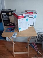 Wooden folding tray table with items on top including two boxed Sunbeam lamps and a boxed flameless candle, plus flashlight and key fob.