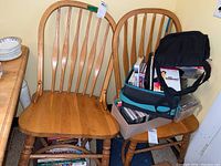 Pair of wooden dining chairs with light natural finish, showing contoured seats, vertical spindle backrests, turned legs with crossbar supports. Chairs need cleaning.