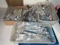 Four containers of assorted flatware including one original box labeled Community Silverplate and two plastic bins with loose silver plated silverware.