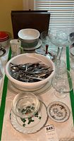 Wide shot showing the white bowl filled with flatware, glass goblet, bowls, decorative plate, and shaker