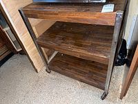 Front view of metal kitchen cart showing three wood-finished shelves and metal frame on wheels.