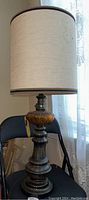 Full view of the vintage lamp showing the wooden base, amber glass accent, and stained off-white fabric cylindrical shade with dark trim.