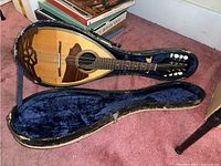 Mandolin resting inside an open hard case lined with blue plush fabric.