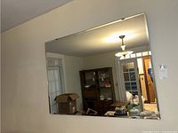 Large rectangular beveled wall mirror mounted on interior wall, reflecting a room with wooden shelving and light fixture.