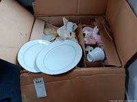 Box with multiple Noritake china pieces including plates and cups, packed in cardboard and wrapped in paper.