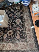 Full view of Oriental style area rug with black field and beige border, placed amid household items.