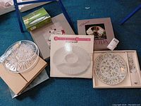 Image of assorted serving platters, boxes showing a crystal clear chip and dip tray, California Classics chip and dip tray, and Andrea by Sadek cake service box with ceramic floral pieces.