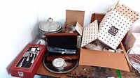 Overview of various silverplated, stainless, and pewter serving ware including boxed utensils, tray, and pitchers