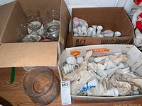 Three cardboard boxes containing clear glass vases and bowls, plus white ceramic vases and candlestick holders, some wrapped in paper and visibly dirty.