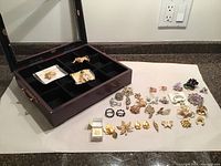 Wide view of wooden case with velvet lining and multiple vintage costume jewellery brooches laid out alongside the case.