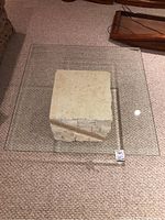 Square coffee table with thick bevelled glass top visible from above, showing a heavy clear glass surface and beige faux stone base inside.