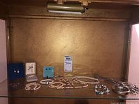 Multiple pieces of costume jewellery including pearl necklaces, bracelets, earrings on display, and chains arranged on a shelf with a golden background.
