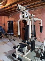 Full view of white frame multi-station gym machine with bench, weight stack and various pulleys