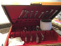 Full view of the open wooden box lined with red velvet holding knives and some spoons and forks in their slots.