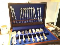 Overview of complete flatware set arranged inside open wooden box lined with blue velvet