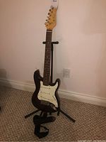 Full view of the electric guitar standing on a black stand, showing the body, neck, and strap attached.