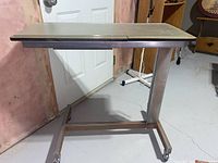 Side view of hospital bed table on casters with glass top.