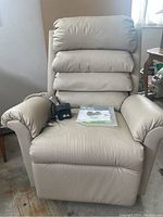 Front view of beige electric lift chair with remote and manual on seat